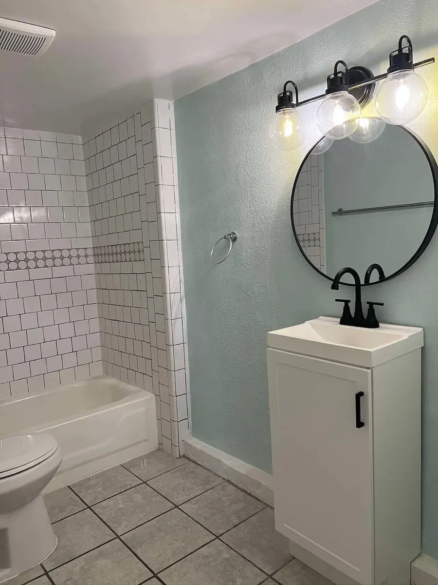 Rental bathroom with teal accent wall, round mirror and white vanity after cleaning
