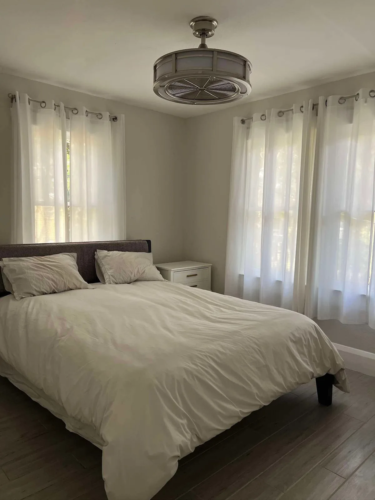 Clean bedroom with white bedding and sheer curtains after recurring clean